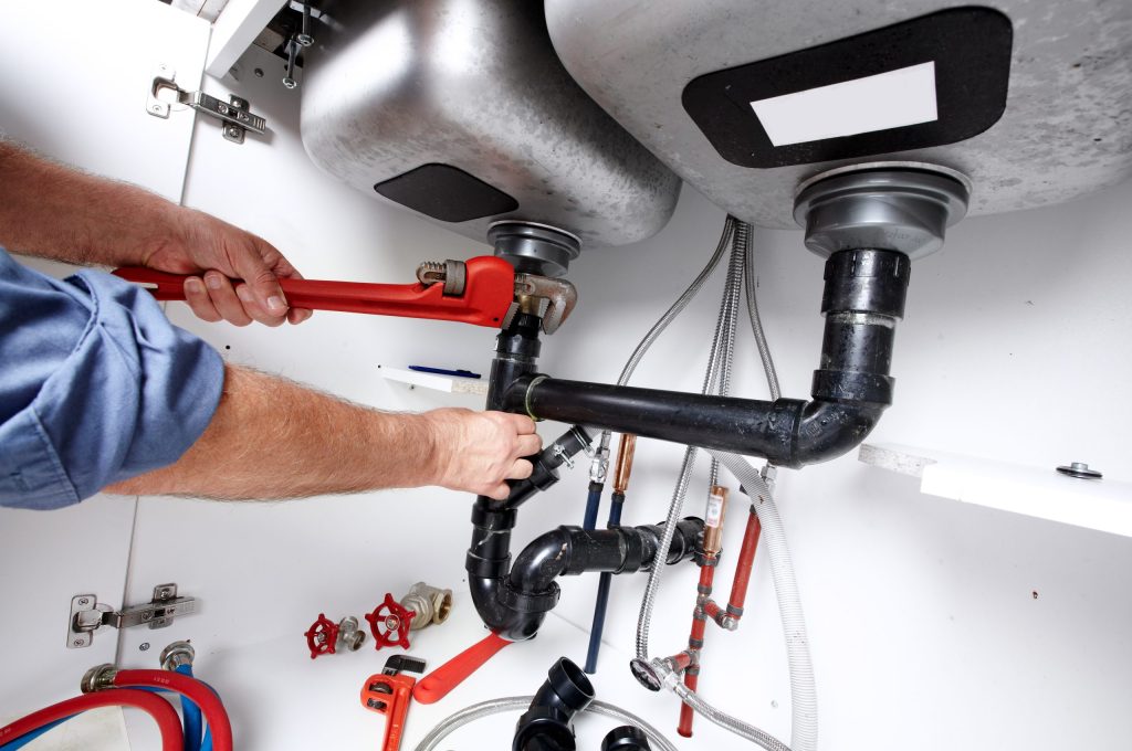 Hands of professional Plumber with a wrench. Clogged sink.